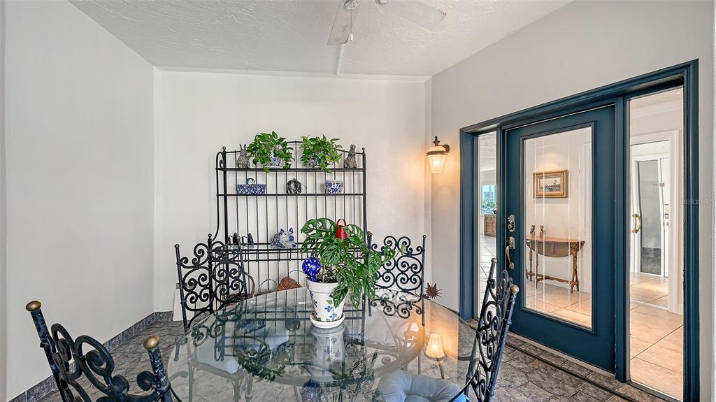 A sunroom features a glass-topped table, a metal baker's rack, and dark blue-framed glass doors — 660 GOLDEN GATE POINT UNIT 51 & 52, SARASOTA, FL