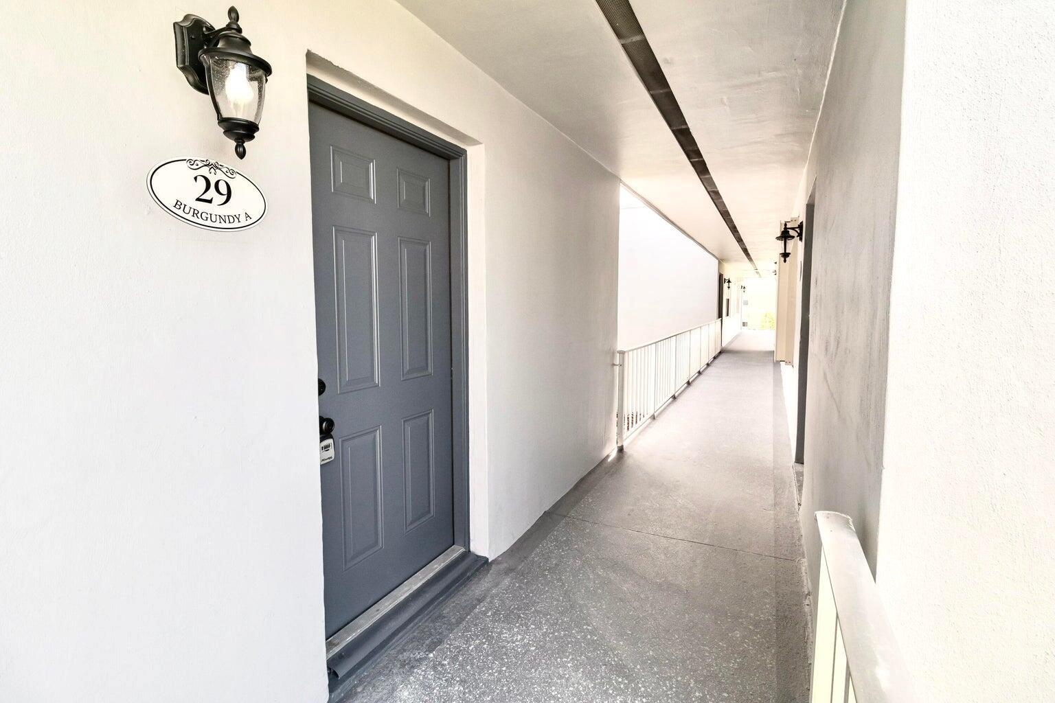 A gray door with a house number plaque sits along an outdoor apartment hallway — 29 Burgundy A, Delray Beach FL 33484, DELRAY BEACH, FL