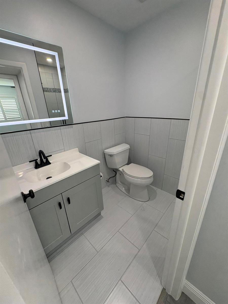 A small bathroom features a gray vanity, a toilet, and light gray tiled walls — 29 Burgundy A, Delray Beach FL 33484, DELRAY BEACH, FL