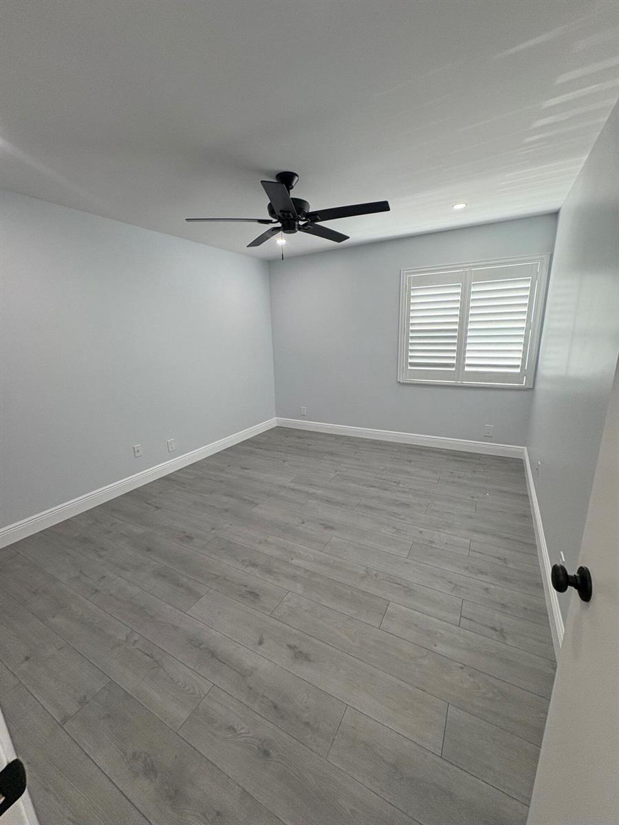 An empty bedroom features light gray walls, wood-look flooring, a ceiling fan, and window shutters — 29 Burgundy A, Delray Beach FL 33484, DELRAY BEACH, FL