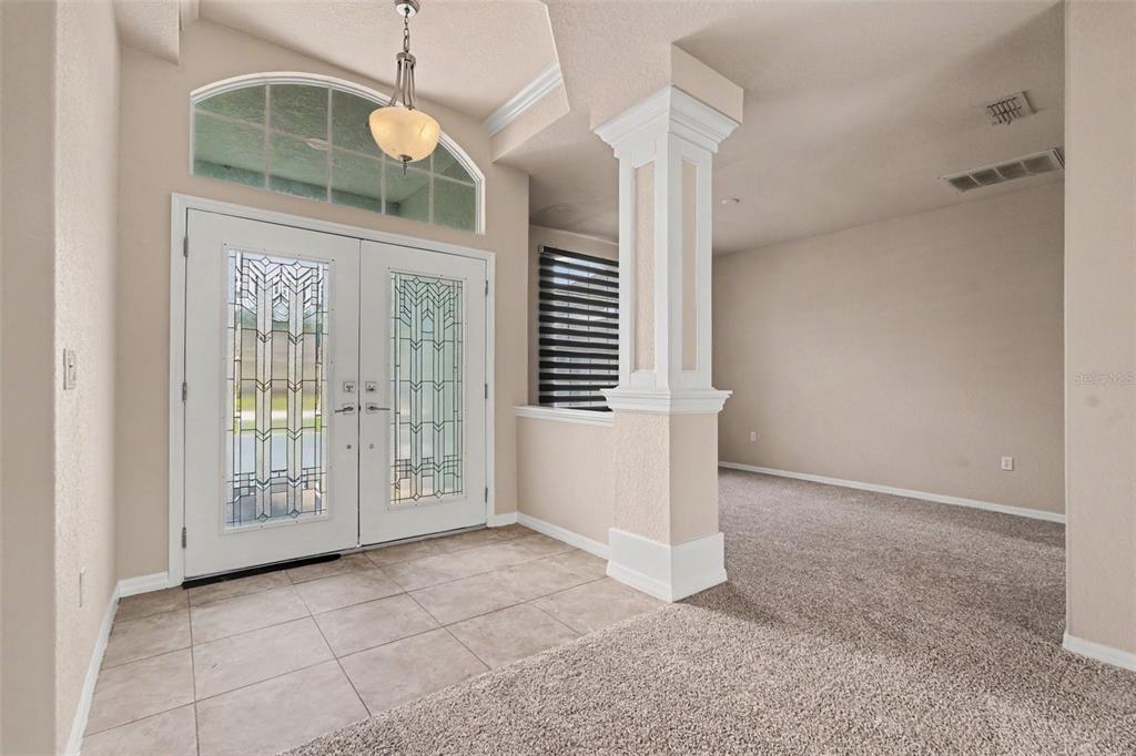 An entryway features a tiled floor, double glass-paneled doors, a column, and carpeted flooring — 5020 GEVALIA DRIVE, BROOKSVILLE, FL