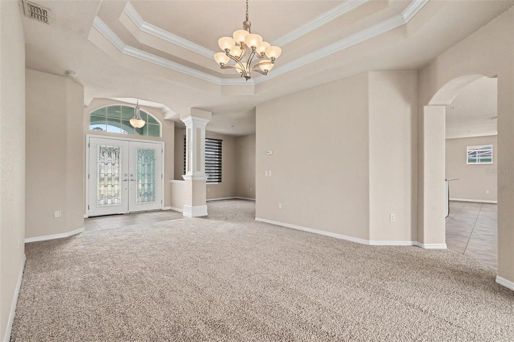 A carpeted living room features a tray ceiling, a chandelier, and an arched entryway — 5020 GEVALIA DRIVE, BROOKSVILLE, FL