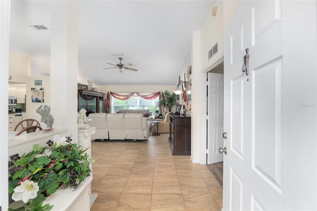 A view from an open front door into a tiled living room with vaulted ceilings — 11563 SW 74TH COURT, OCALA, FL