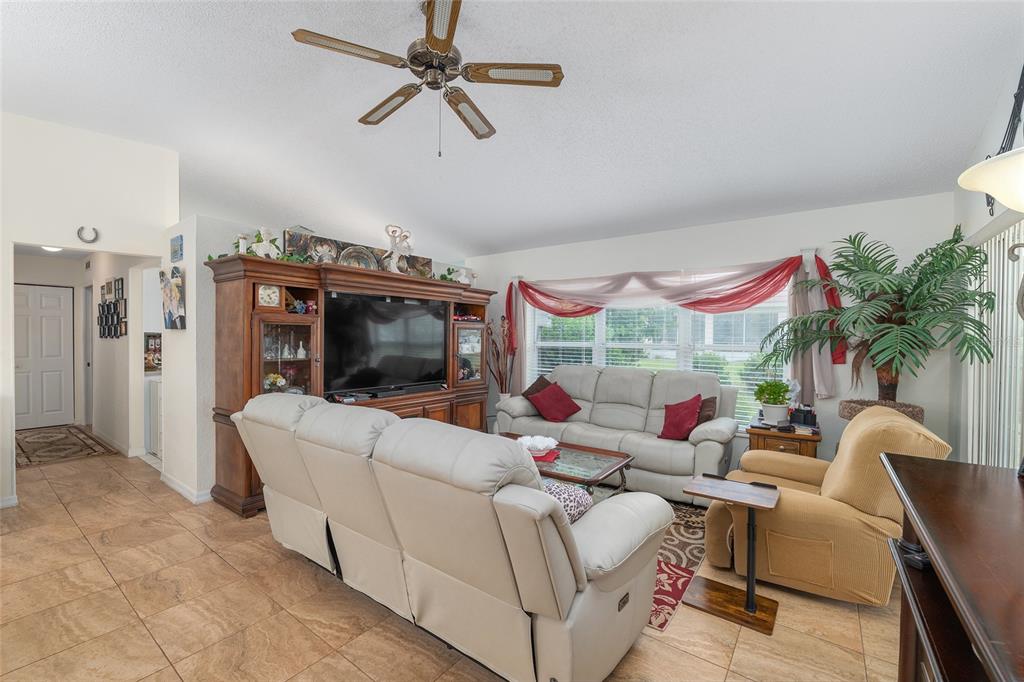 A living room features tile flooring, a ceiling fan, a large entertainment center, and seating — 11563 SW 74TH COURT, OCALA, FL