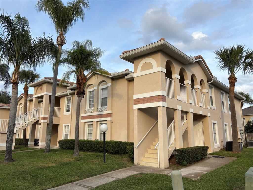 A two-story tan stucco apartment building features palm trees, exterior staircases, and balconies — 13301 FAIRWAY GLEN DRIVE UNIT 104, ORLANDO, FL