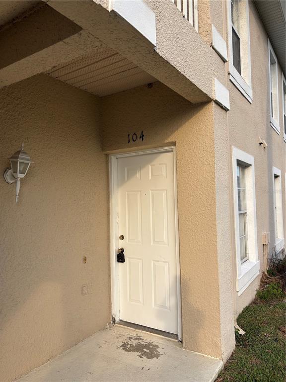 A white front door with a lockbox is set into a beige stucco building exterior — 13301 FAIRWAY GLEN DRIVE UNIT 104, ORLANDO, FL