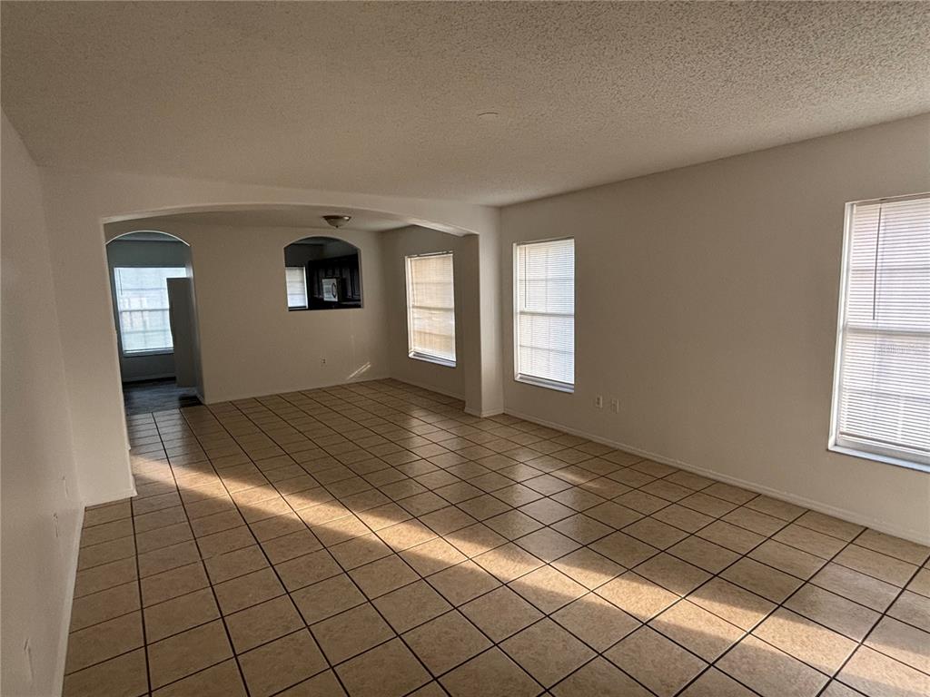 An empty living room features light-colored tile flooring, white walls, and several windows with blinds — 13301 FAIRWAY GLEN DRIVE UNIT 104, ORLANDO, FL