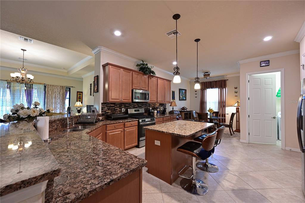 A kitchen with granite countertops, wooden cabinets, a center island, and two bar stools — 13423 RAMBLEWOOD TRAIL, BRADENTON, FL