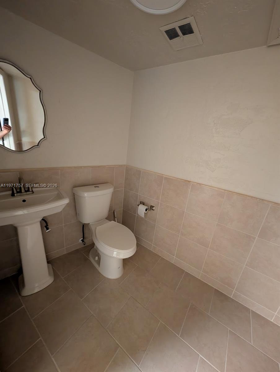 A bathroom features a pedestal sink, a toilet, and beige wall and floor tiles — 801 S Dixie Hwy W, Pompano Beach FL 33060, POMPANO BEACH, FL