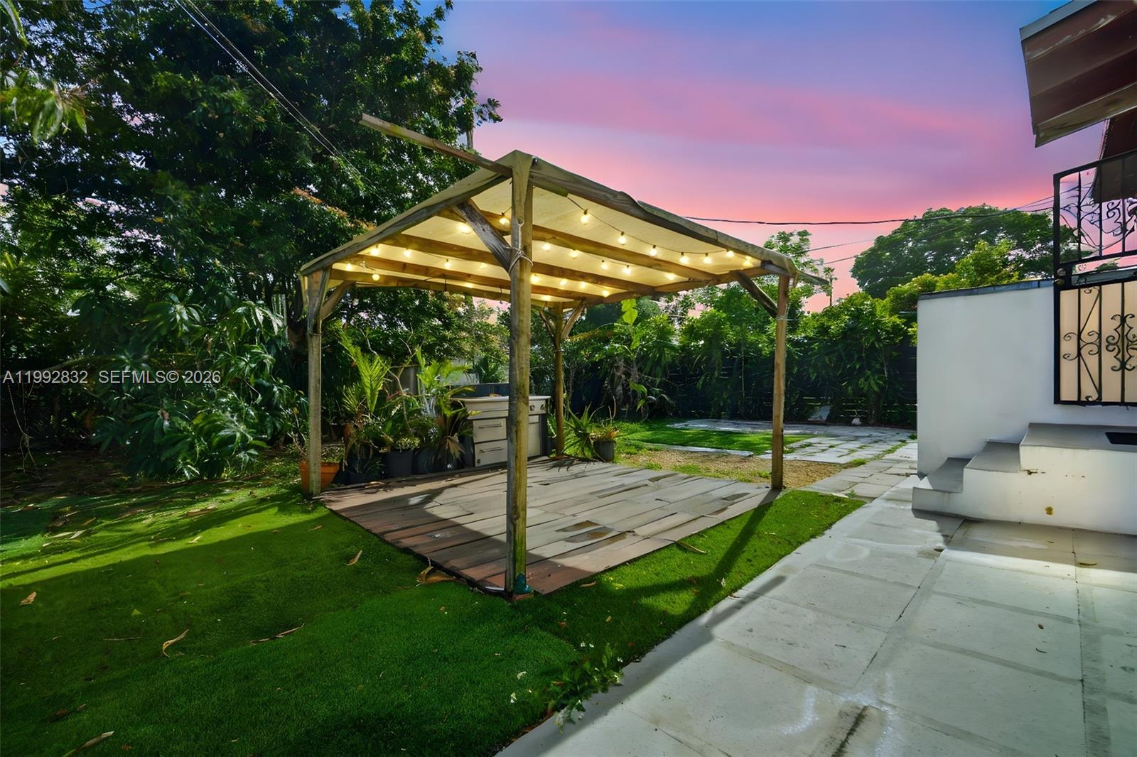A wooden pergola with string lights stands over a deck in a grassy backyard — 6336 SW 9th St, West Miami FL 33144, WEST MIAMI, FL
