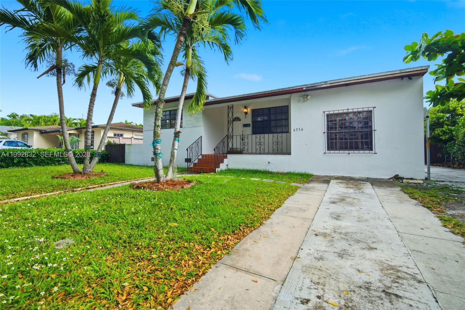 A single-story white house features a front lawn, palm trees, and a concrete driveway — 6336 SW 9th St, West Miami FL 33144, WEST MIAMI, FL
