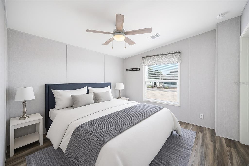 A bedroom features a bed with a blue headboard, gray bedding, and a ceiling fan — 1 BEAVERKILL DRIVE, LAKE WALES, FL