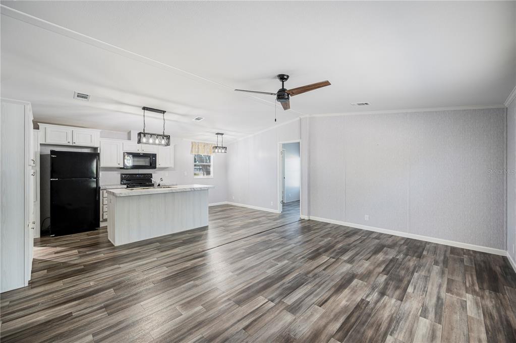 An open-concept kitchen and living area featuring white cabinets, a kitchen island, and wood-look flooring — 1 BEAVERKILL DRIVE, LAKE WALES, FL
