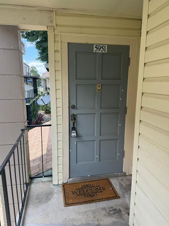A gray front door with a lockbox and a welcome mat on a concrete porch — 5951 VILLAGE CIRCLE UNIT GE, ORLANDO, FL