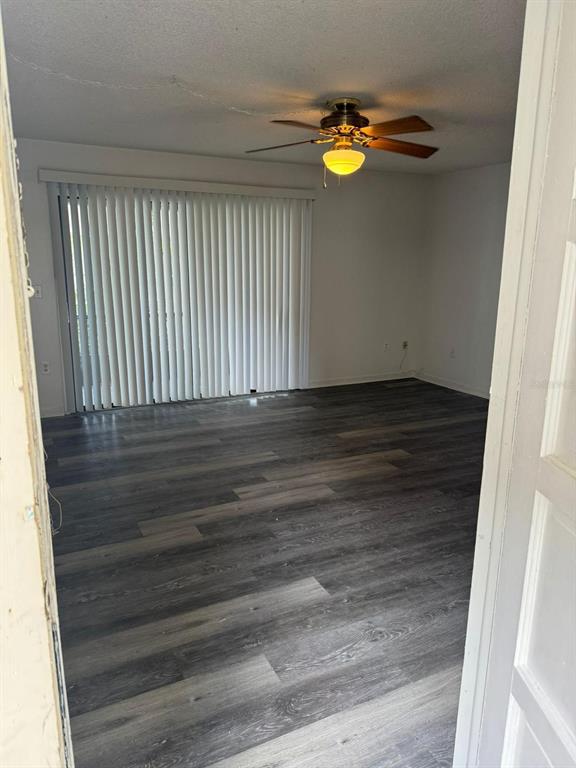 An empty room features gray wood-look flooring, a ceiling fan, and vertical blinds on sliding doors — 5951 VILLAGE CIRCLE UNIT GE, ORLANDO, FL