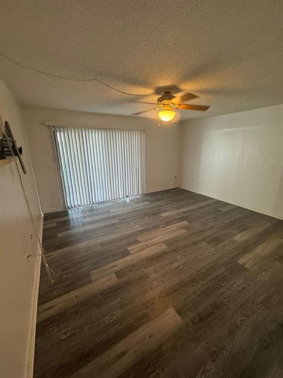 An empty room features wood-look flooring, a ceiling fan, and vertical blinds on a sliding door — 5951 VILLAGE CIRCLE UNIT GE, ORLANDO, FL