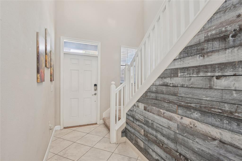 An entryway features a white door, tiled floor, and a staircase with a wood-plank accent wall — 1537 TALLULAH TERRACE, WESLEY CHAPEL, FL