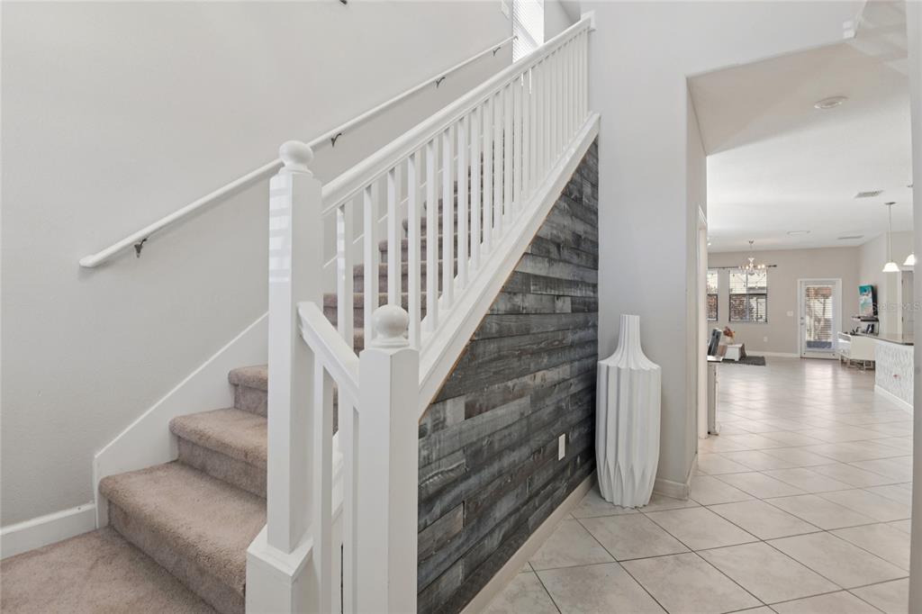 A staircase with carpeted steps and a white railing sits beside a wood-paneled accent wall — 1537 TALLULAH TERRACE, WESLEY CHAPEL, FL