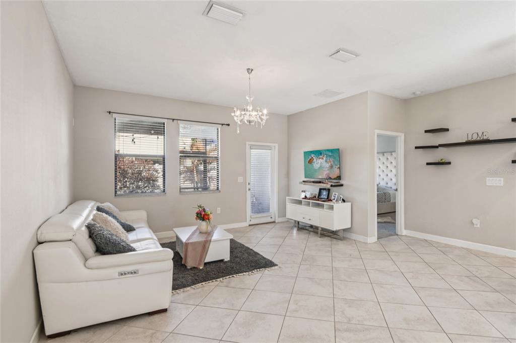 A living room features light tile floors, a white sofa, a coffee table, and a chandelier — 1537 TALLULAH TERRACE, WESLEY CHAPEL, FL