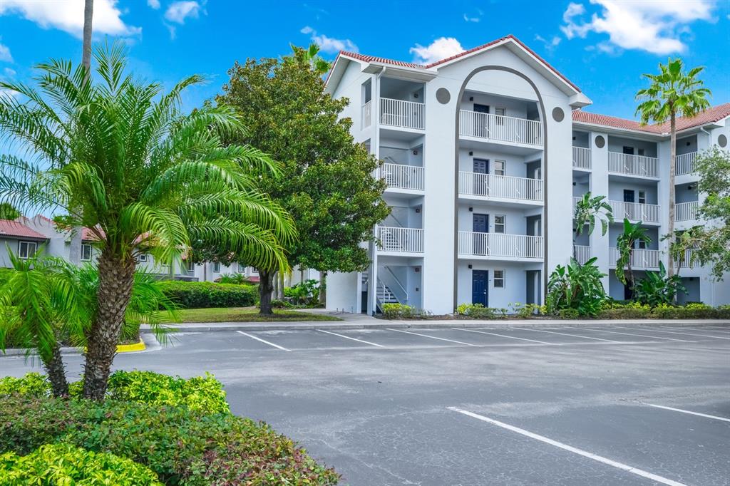 A multi-story apartment building with white stucco walls and balconies sits behind a parking lot — 2954 SADINA STREET UNIT Tower 3, KISSIMMEE, FL