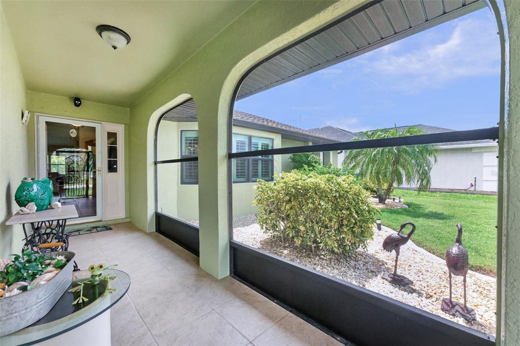 A covered patio with tiled flooring features a screened-in wall overlooking a landscaped backyard — 25636 AYSEN DRIVE, PUNTA GORDA, FL