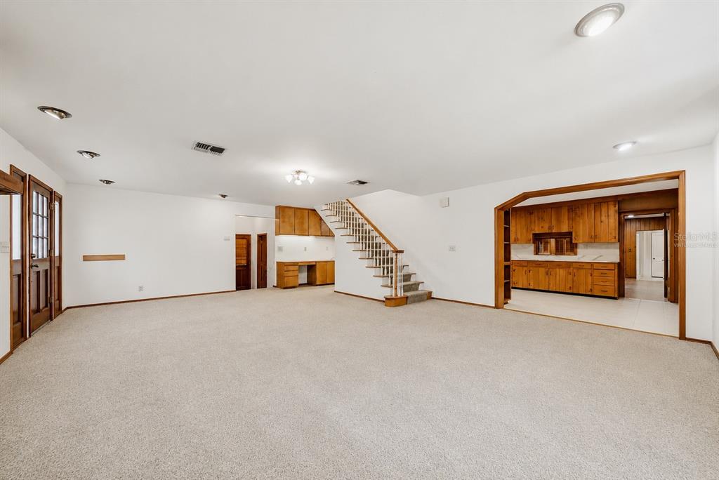 A large carpeted living room features a wooden staircase, recessed lighting, and an adjacent kitchen — 3123 W OAKLYN AVENUE, TAMPA, FL