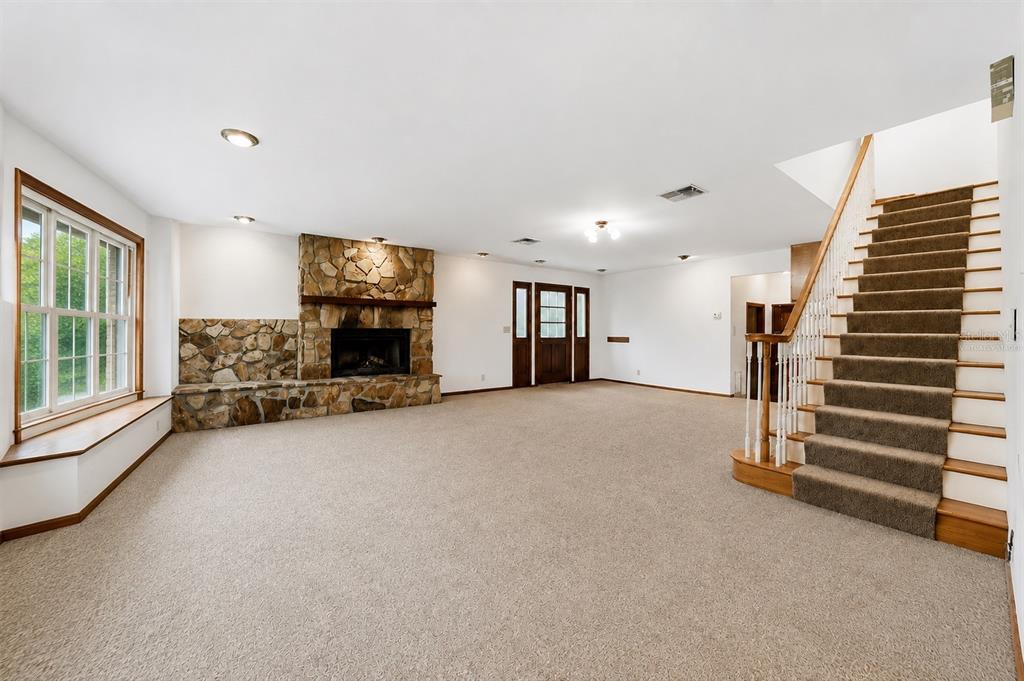 A spacious living room features a stone fireplace, carpeted flooring, and a staircase with wooden railings — 3123 W OAKLYN AVENUE, TAMPA, FL