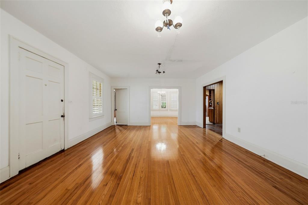 A bright, empty room features polished hardwood floors, white walls, and multiple doorways — 3123 W OAKLYN AVENUE, TAMPA, FL
