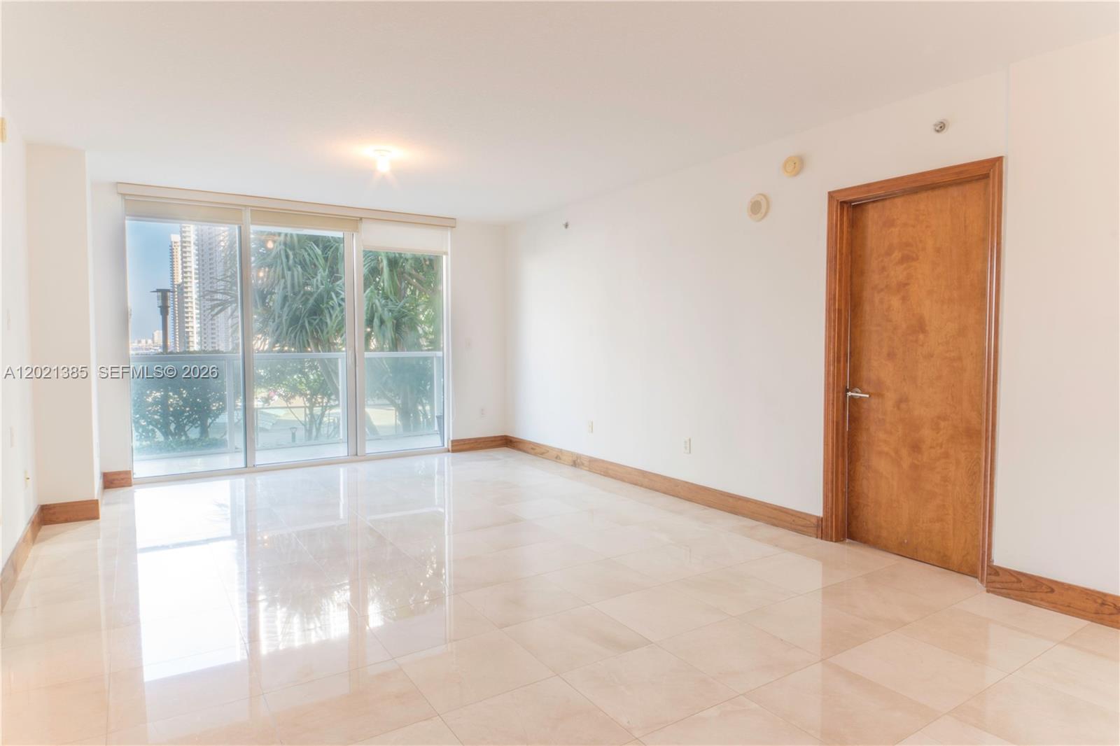 An empty room features white walls, light-colored tile flooring, wood baseboards, and a sliding glass door — 31 SE 5th St # 1208, Miami FL 33131, MIAMI, FL