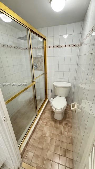 A bathroom features a glass-enclosed shower with gold trim, a white toilet, and tiled flooring — 2025 NE 164th St # 616, North Miami Beach FL 33162, NORTH MIAMI BEACH, FL