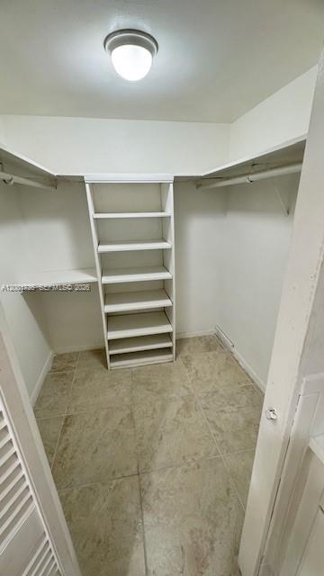 A walk-in closet features white shelving, hanging rods, and light-colored tile flooring — 2025 NE 164th St # 616, North Miami Beach FL 33162, NORTH MIAMI BEACH, FL