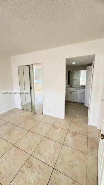 A bedroom with beige tile flooring, mirrored closet doors, and an open doorway to a bathroom — 2025 NE 164th St # 616, North Miami Beach FL 33162, NORTH MIAMI BEACH, FL