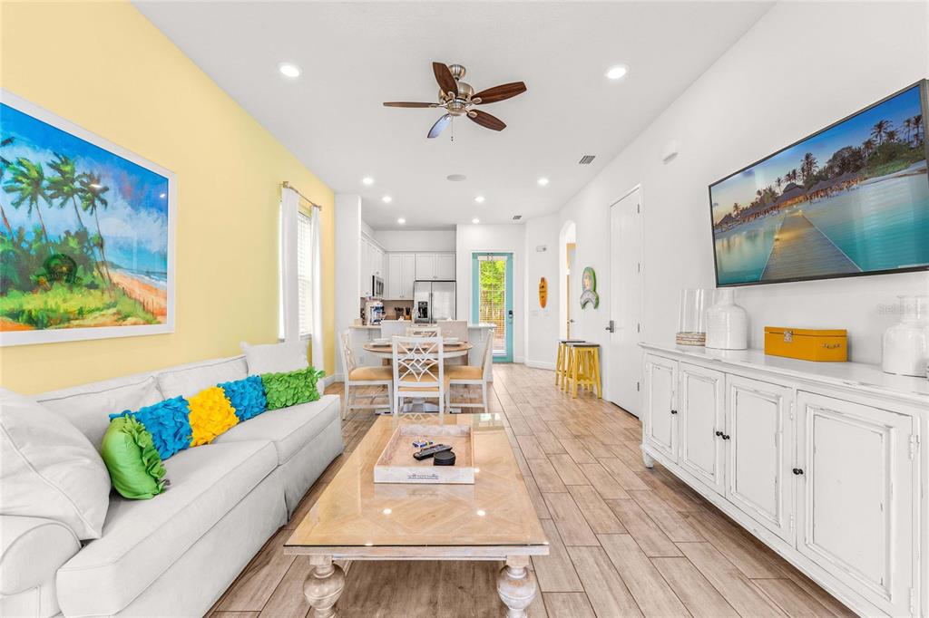 A bright living room features a white sofa, glass coffee table, and a wall-mounted television — 8005 SAND BAR DRIVE, KISSIMMEE, FL