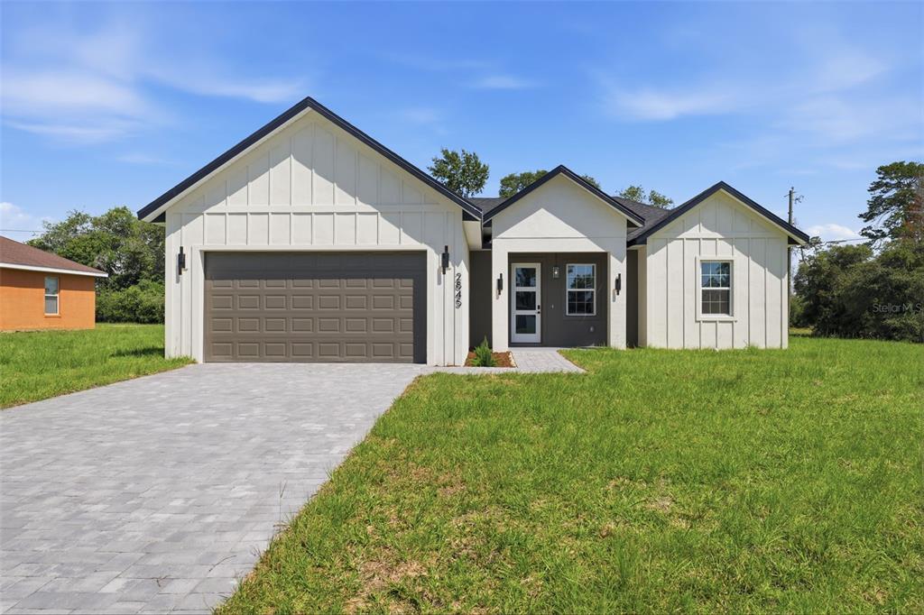 A modern single-story house with white board-and-batten siding, a gray garage door, and a paved driveway — 2845 SW 172ND LANE ROAD, OCALA, FL