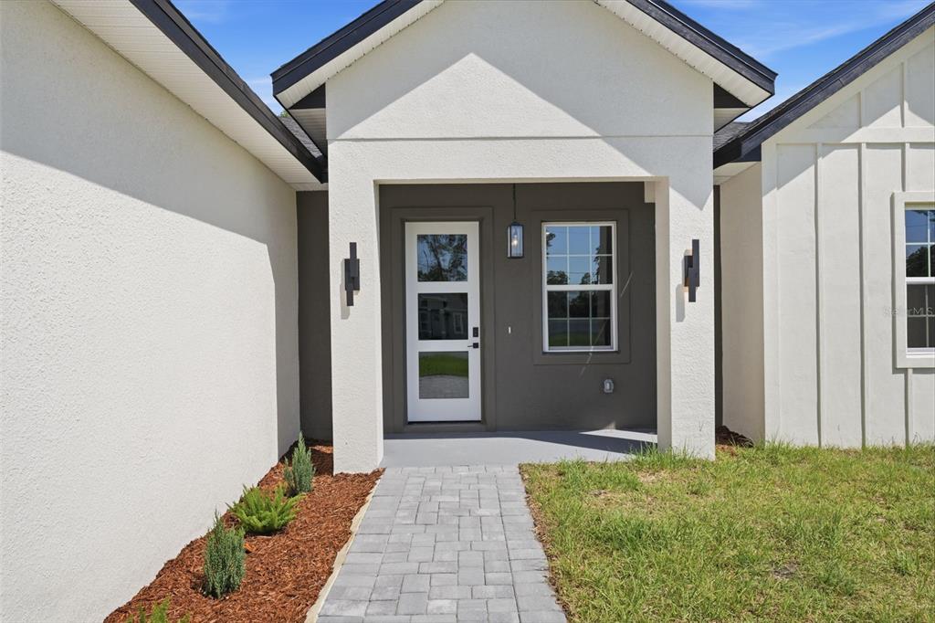 A paved walkway leads to the covered entryway of a modern home with white stucco — 2845 SW 172ND LANE ROAD, OCALA, FL