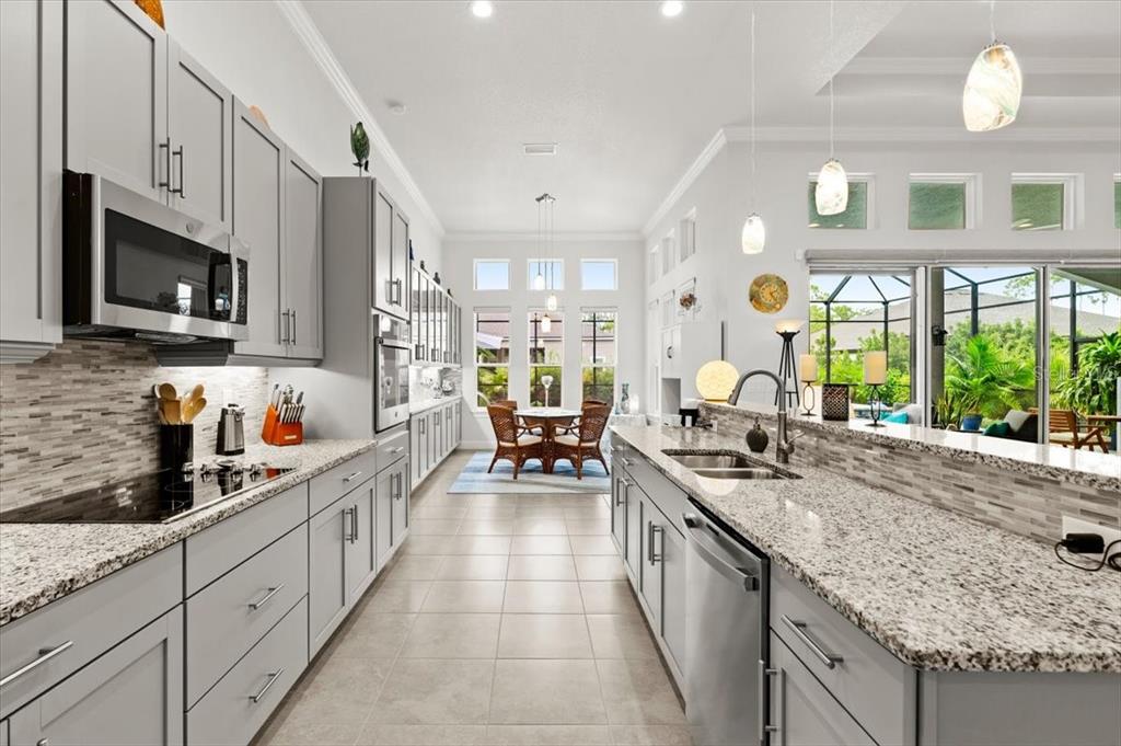 A modern kitchen features gray cabinets, granite countertops, and a dining area with large windows — 2426 WILD TURKEY CREEK LN, PORT ORANGE, FL
