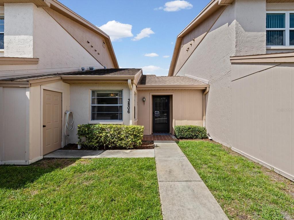A beige townhouse exterior features a concrete walkway leading to a front door and window — 3806 STAYSAIL LANE, HOLIDAY, FL