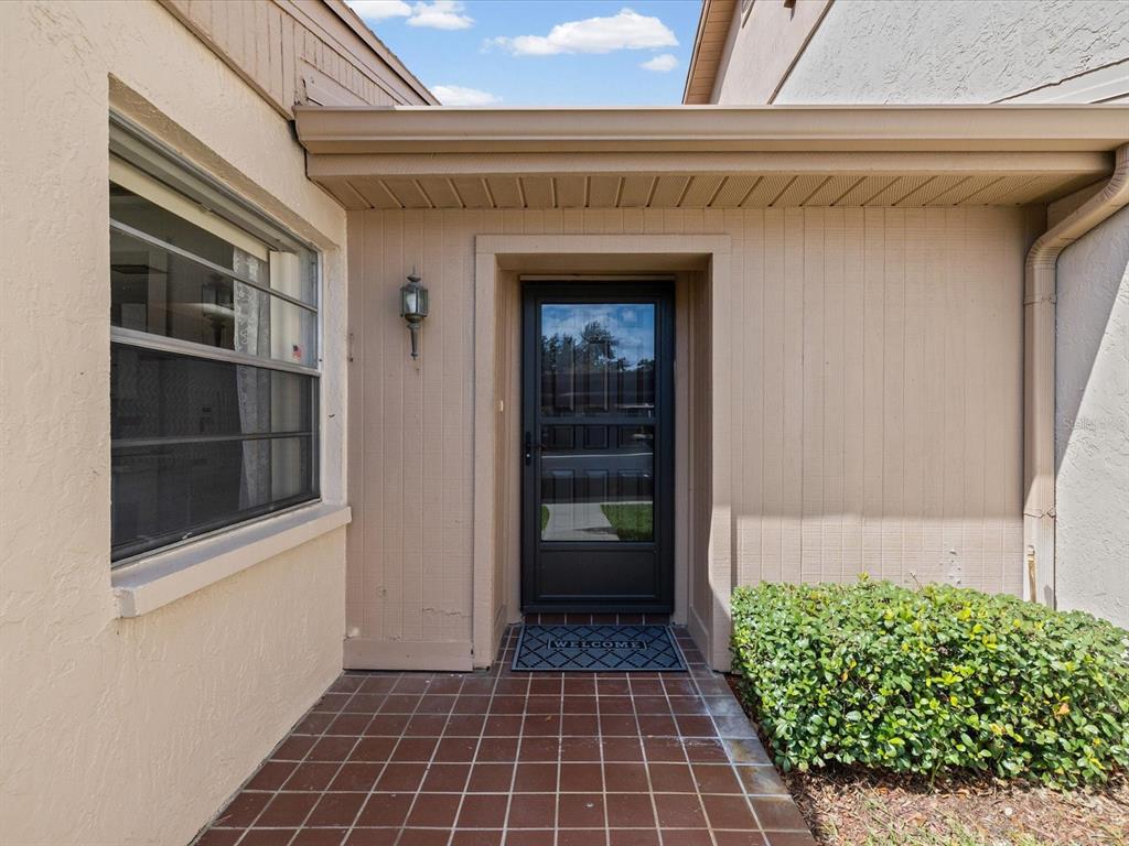 A front entryway features a tiled porch, a dark storm door, and a small bush — 3806 STAYSAIL LANE, HOLIDAY, FL