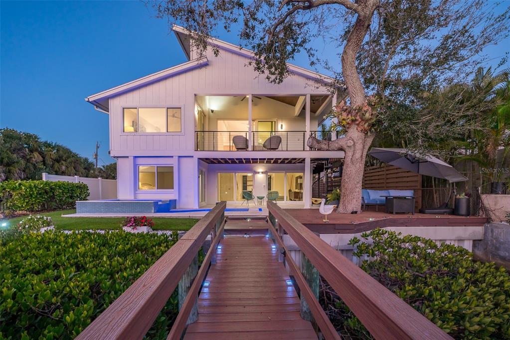 A wooden footbridge leads to a two-story house with a pool and a large tree — 4938 COMMONWEALTH DRIVE, SARASOTA, FL