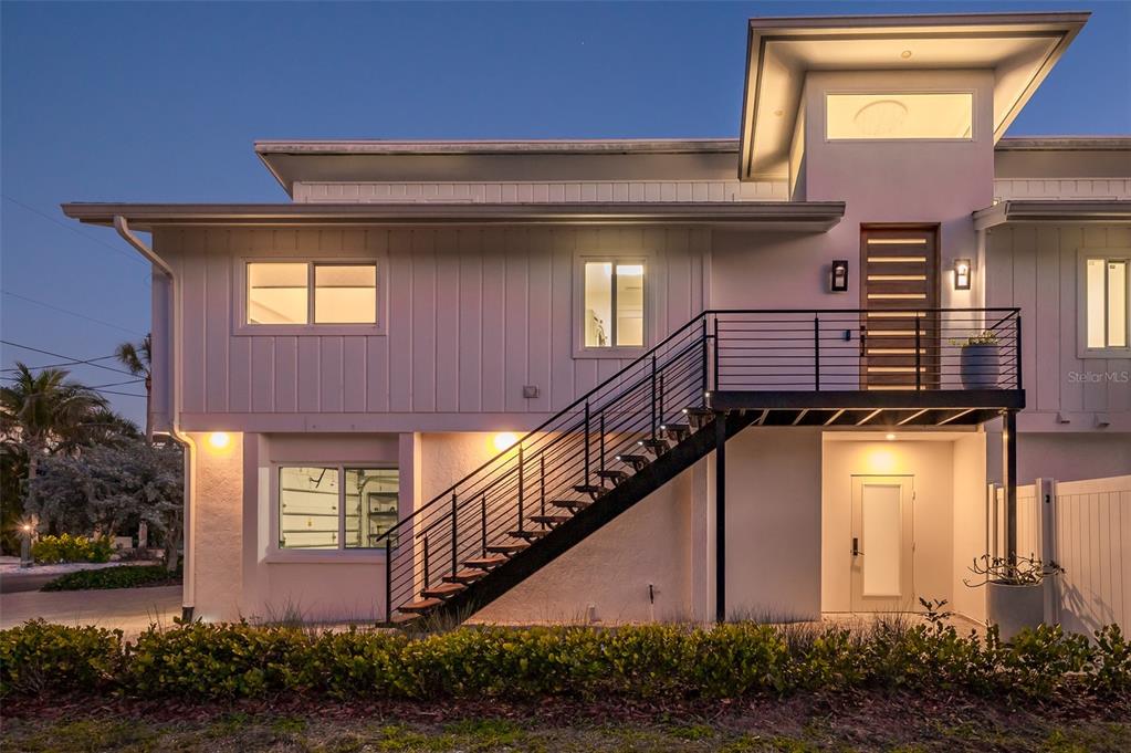 A two-story house exterior features white vertical siding, an outdoor staircase, and a front door — 4938 COMMONWEALTH DRIVE, SARASOTA, FL