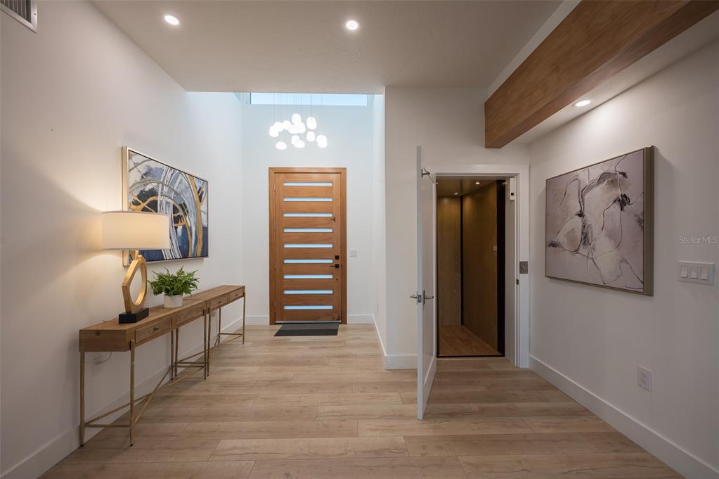 A modern entryway features light wood flooring, a wooden front door, and a private elevator — 4938 COMMONWEALTH DRIVE, SARASOTA, FL