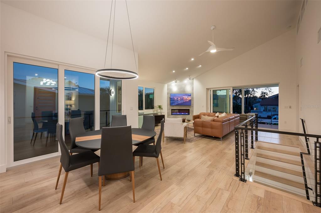 An open-concept living and dining area features light wood floors, a vaulted ceiling, and stairs — 4938 COMMONWEALTH DRIVE, SARASOTA, FL