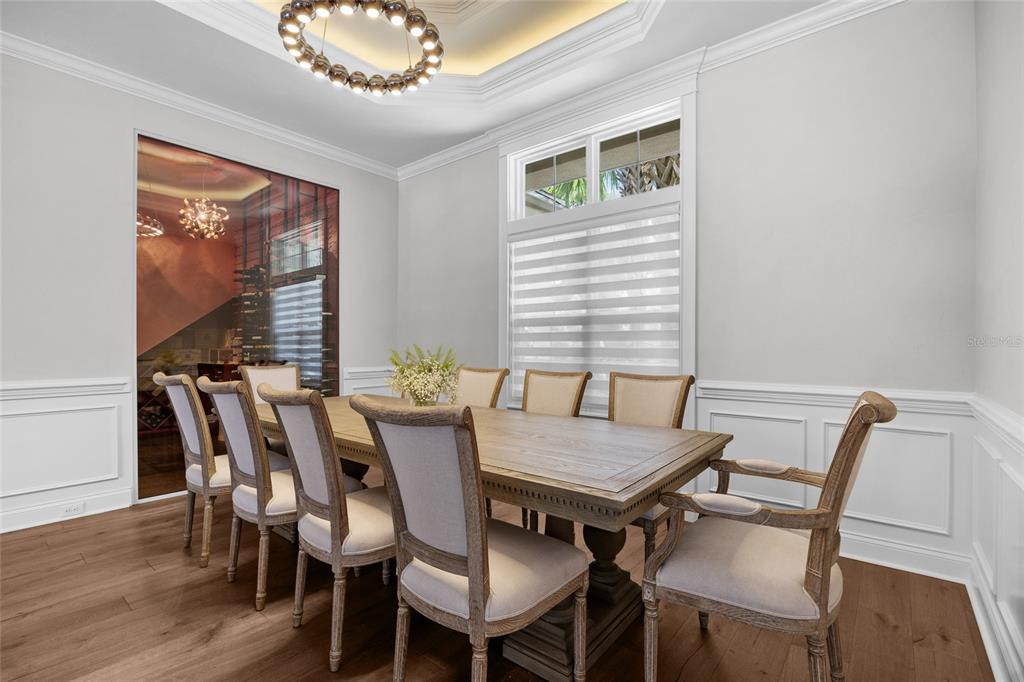 A dining room features a wooden table, upholstered chairs, a chandelier, and a glass-enclosed wine cellar — 11372 SW 30TH AVENUE, GAINESVILLE, FL