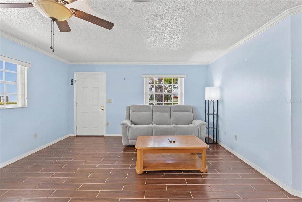 A living room with light blue walls, wood-look tile floors, a sofa, and a coffee table — 6643 KELSEY LANE UNIT 4B, NEW PORT RICHEY, FL