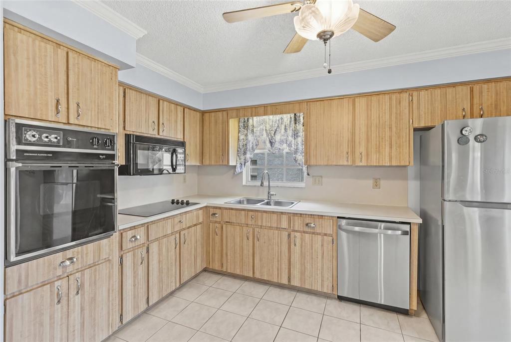 A kitchen features light wood cabinets, stainless steel appliances, a double sink, and tile flooring — 6643 KELSEY LANE UNIT 4B, NEW PORT RICHEY, FL