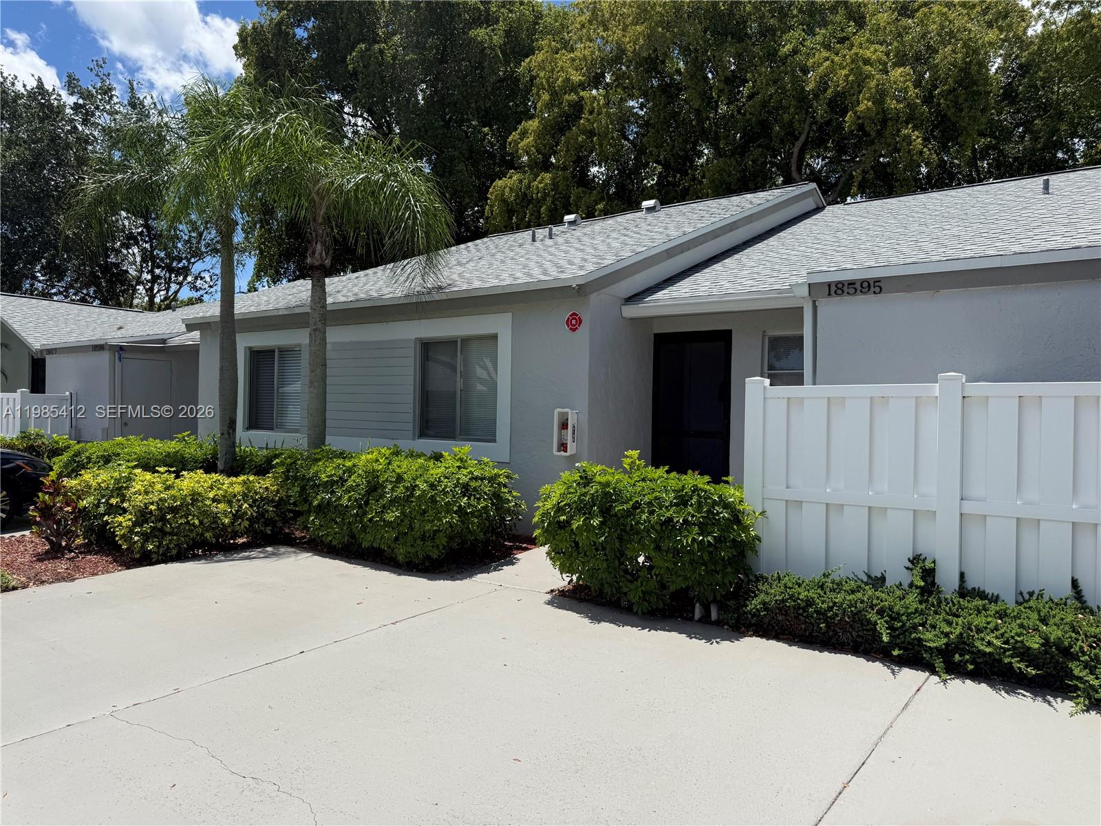 A single-story gray house features a white fence, palm trees, and a concrete driveway — 18595 Egret Way # 18595, Boca Raton FL 33496, BOCA RATON, FL