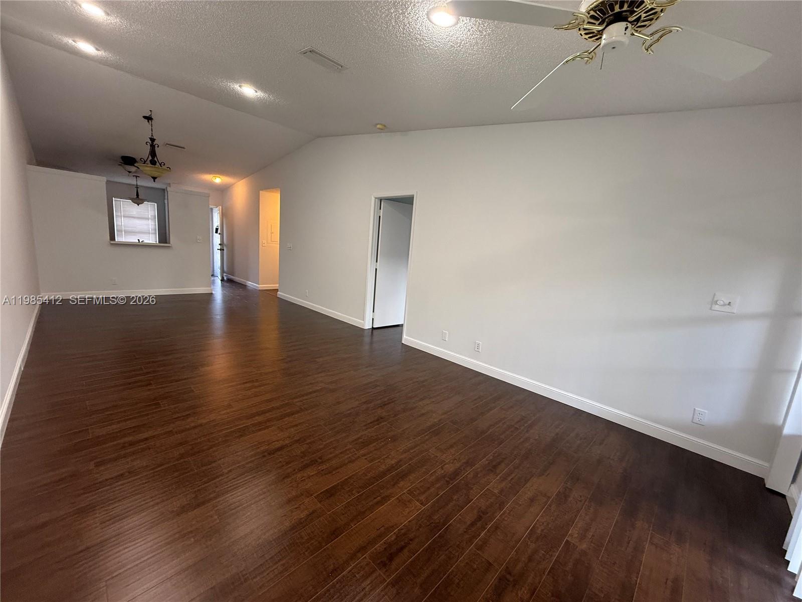 A spacious living area features dark wood-look flooring, white walls, and a vaulted ceiling — 18595 Egret Way # 18595, Boca Raton FL 33496, BOCA RATON, FL