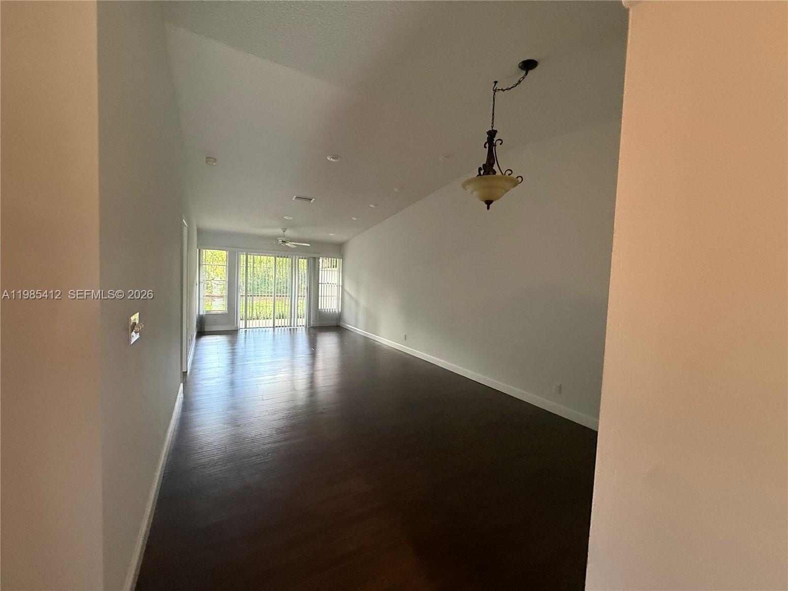 A long, empty living room features dark wood flooring, white walls, and a hanging light fixture — 18595 Egret Way # 18595, Boca Raton FL 33496, BOCA RATON, FL