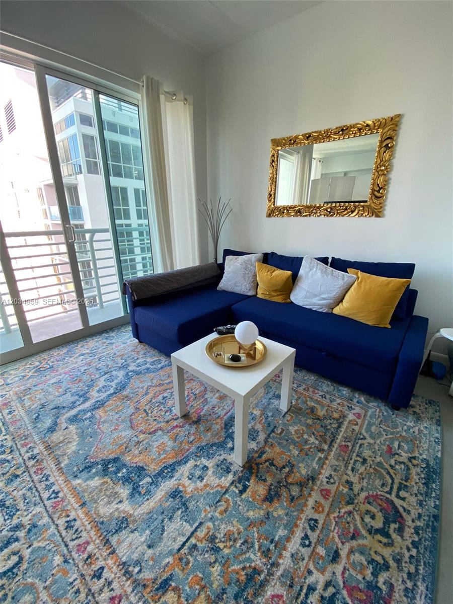 A living room features a blue sectional sofa, a white coffee table, and a patterned rug — 133 NE 2nd Ave # 2805, Miami FL 33132, MIAMI, FL