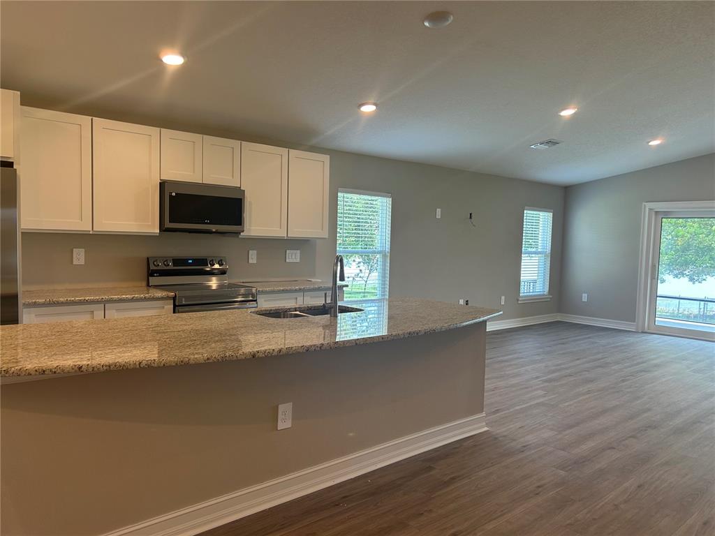 A kitchen with white cabinets, granite countertops, and stainless steel appliances opens to a living area — 373 W MAIN STREET, HAINES CITY, FL